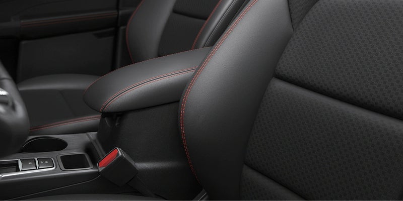 Close-up of a car's black leather or synthetic seats and center console with red contrast stitching.