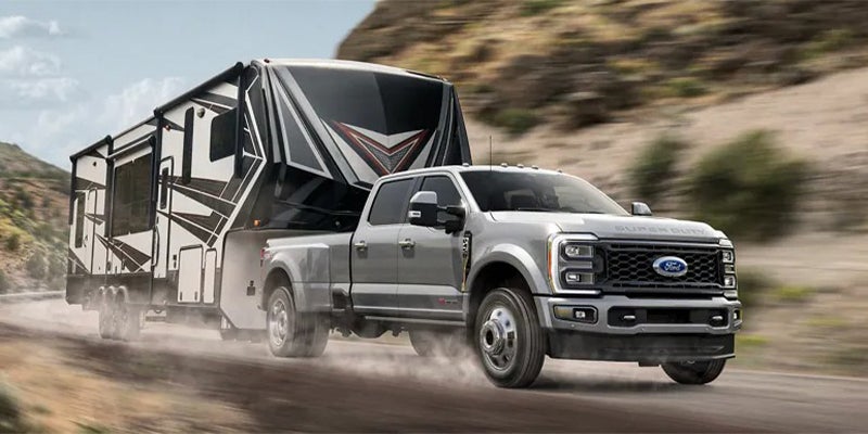 Gray Ford Super Duty dually truck towing a large fifth-wheel RV on a dirt road