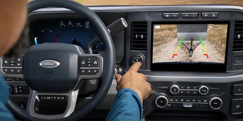 Driver pointing at a touch screen showing a rear view trailer hitch camera with guidance lines