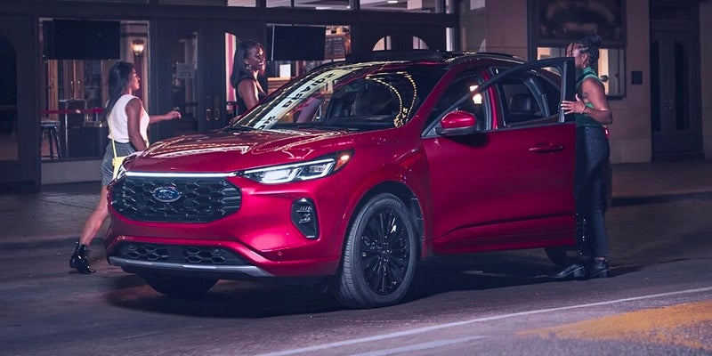 A red Ford Escape SUV is parked at night, with three women near the open doors