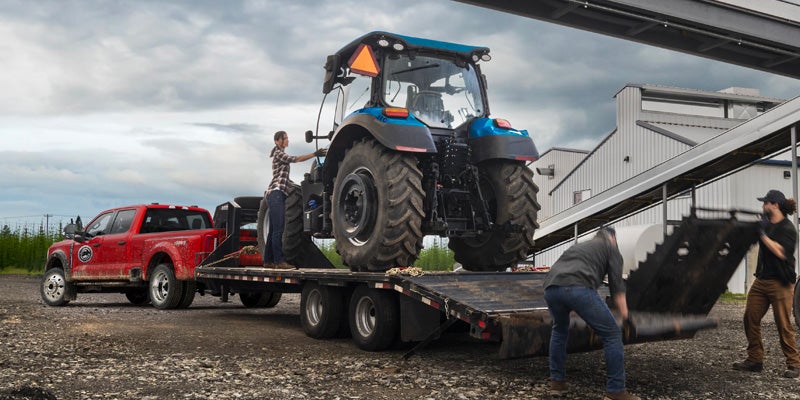 
Red Ford Super Duty dually towing a blue tractor on a large flatbed trailer